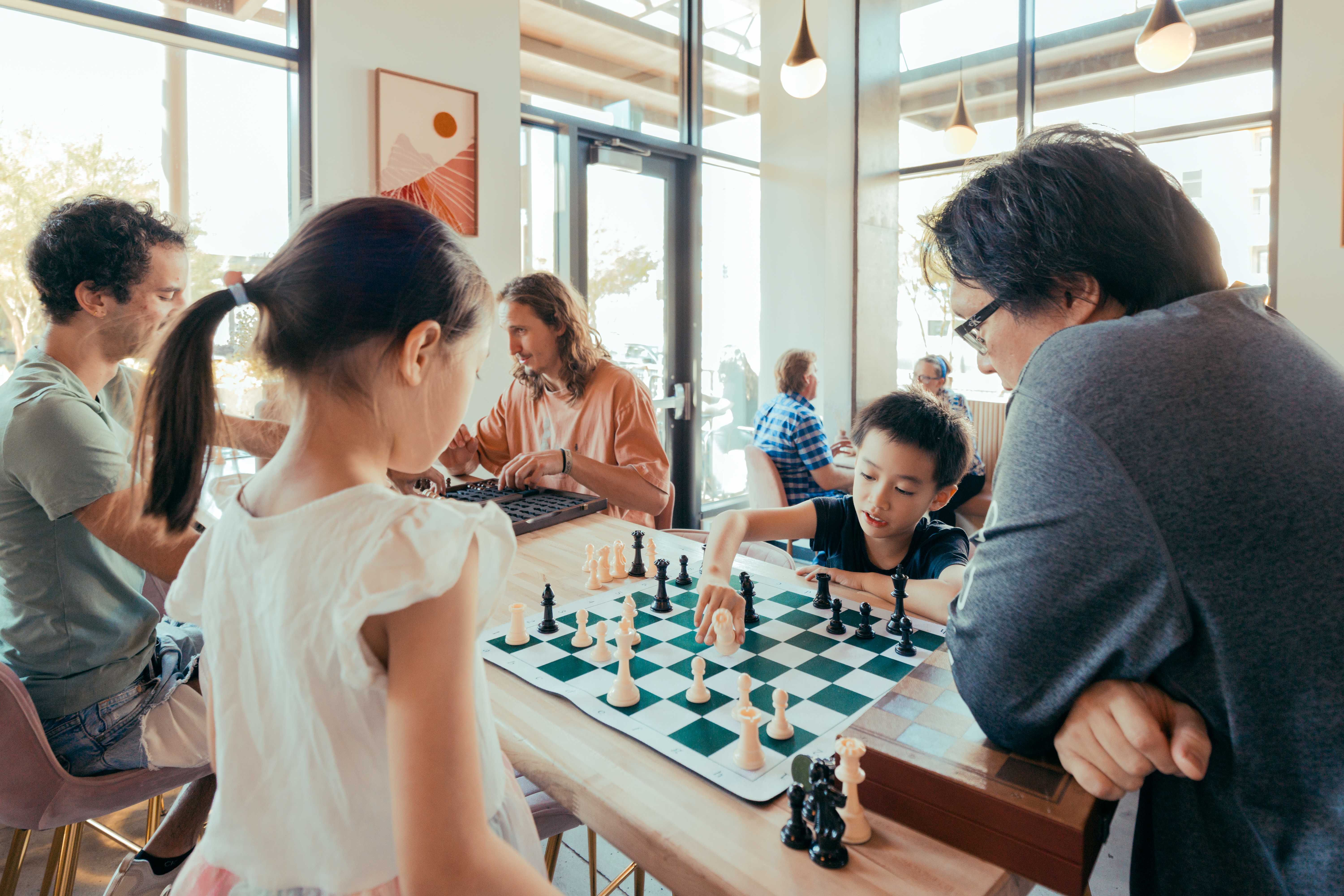 Father watching young son and daughter play chess in coffeeshop